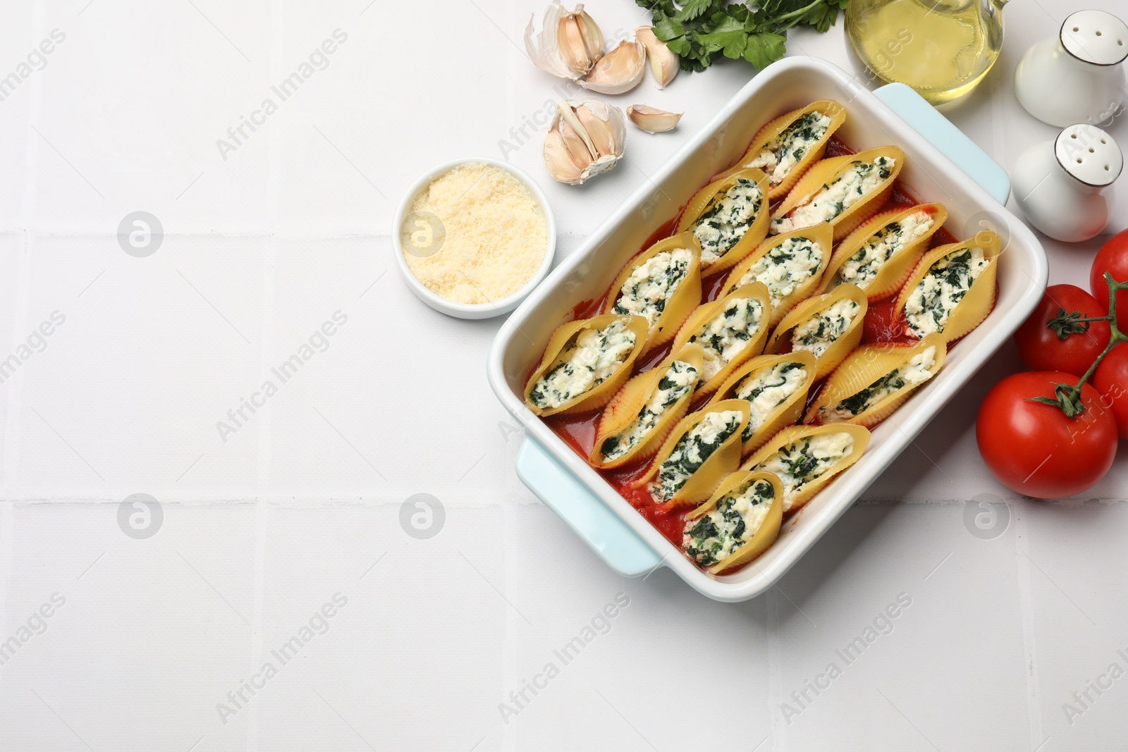 Photo of Delicious conchiglie pasta with ricotta cheese, spinach and tomato sauce in baking dish on white tiled table, flat lay. Space for text