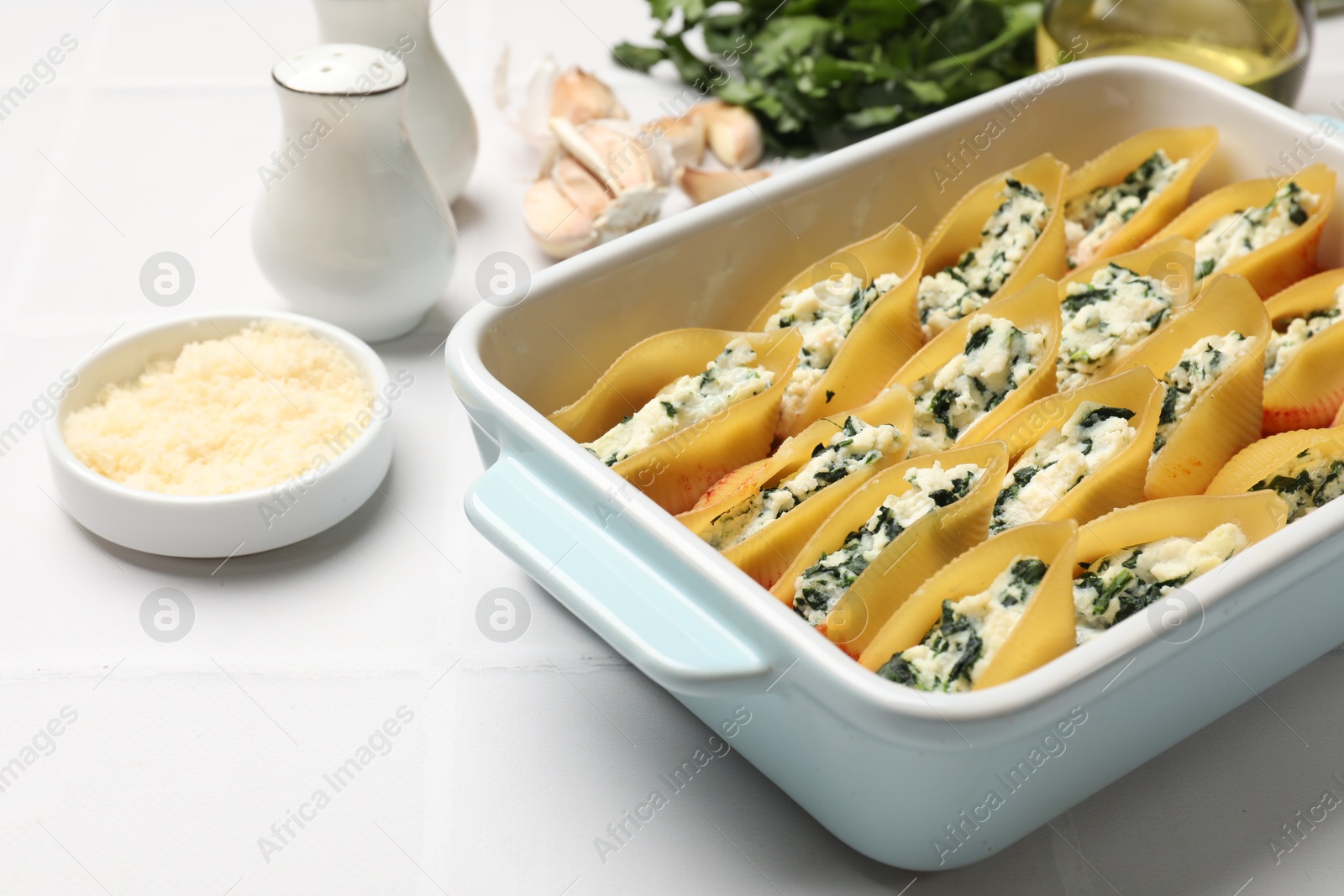 Photo of Delicious conchiglie pasta with ricotta cheese, spinach and tomato sauce in baking dish on light table, closeup