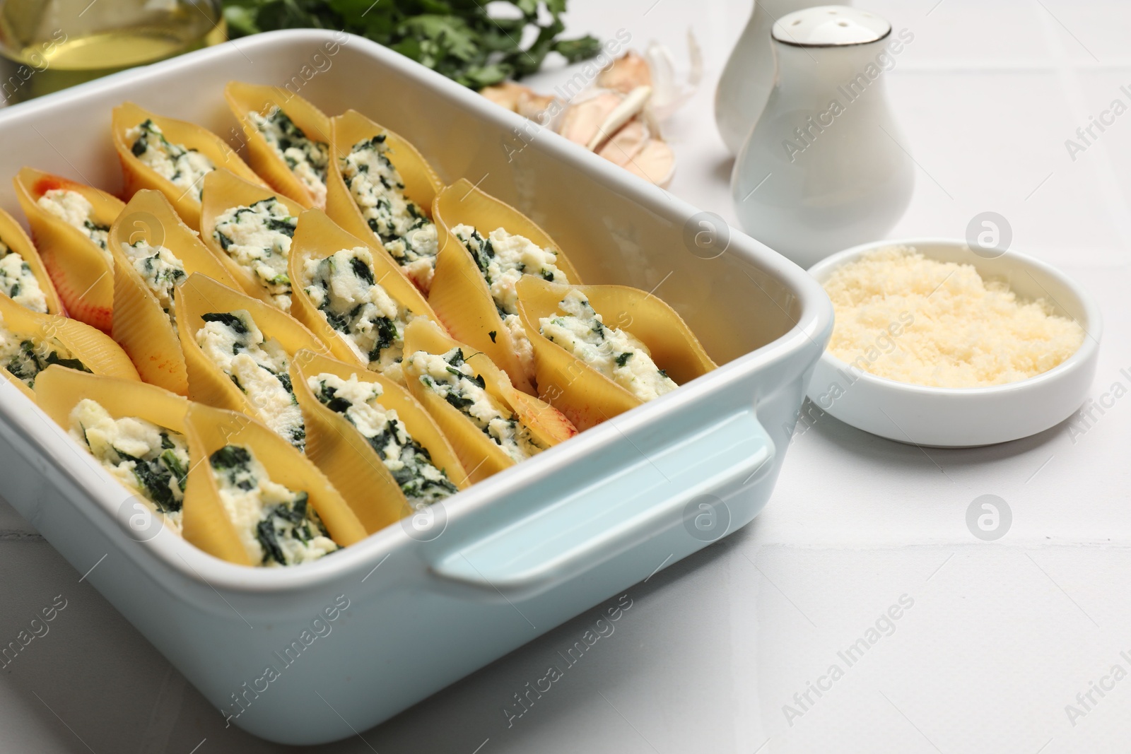 Photo of Delicious conchiglie pasta with ricotta cheese, spinach and tomato sauce in baking dish on light table, closeup