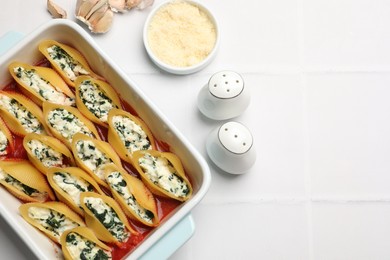 Photo of Delicious conchiglie pasta with ricotta cheese, spinach and tomato sauce in baking dish on white tiled table, flat lay. Space for text