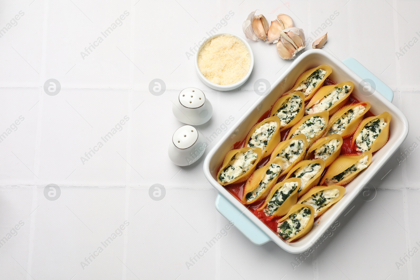 Photo of Delicious conchiglie pasta with ricotta cheese, spinach and tomato sauce in baking dish on white tiled table, flat lay. Space for text