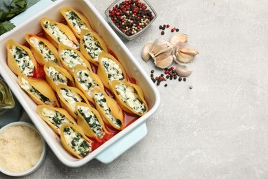 Photo of Delicious conchiglie pasta with ricotta cheese, spinach and tomato sauce in baking dish on gray textured table, flat lay. Space for text