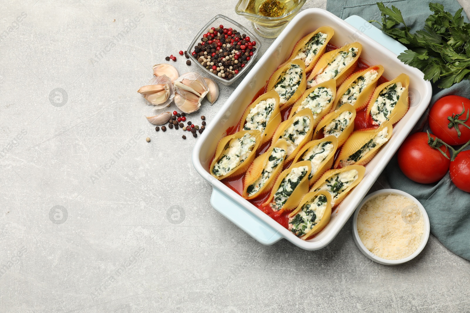 Photo of Delicious conchiglie pasta with ricotta cheese, spinach and tomato sauce in baking dish on gray textured table, flat lay. Space for text