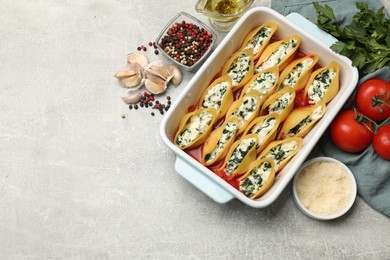 Photo of Delicious conchiglie pasta with ricotta cheese, spinach and tomato sauce in baking dish on gray textured table, flat lay. Space for text