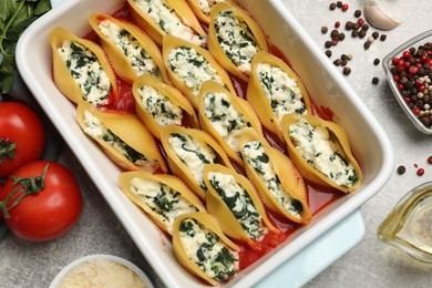 Photo of Delicious conchiglie pasta with ricotta cheese, spinach and tomato sauce in baking dish on gray textured table, flat lay