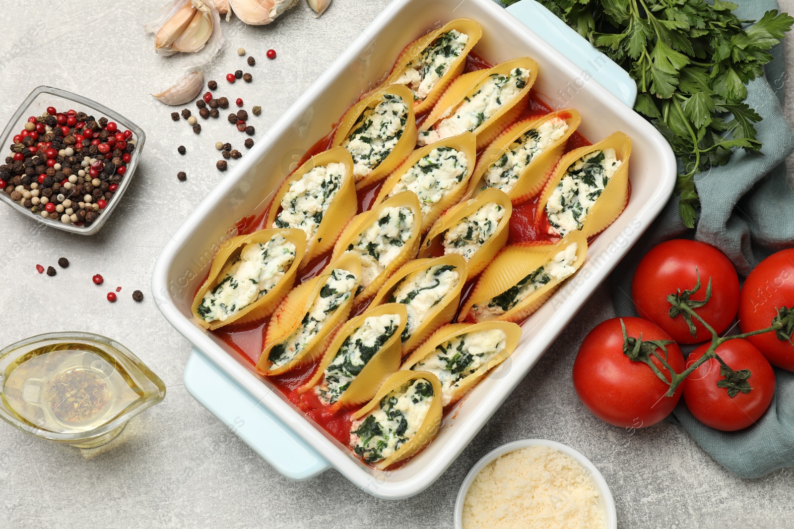 Photo of Delicious conchiglie pasta with ricotta cheese, spinach and tomato sauce in baking dish on gray textured table, flat lay