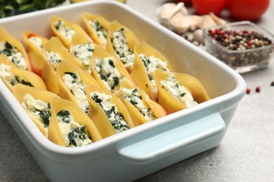 Photo of Delicious conchiglie pasta with ricotta cheese, spinach and tomato sauce in baking dish on gray textured table, closeup