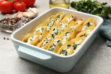 Photo of Delicious conchiglie pasta with ricotta cheese, spinach and tomato sauce in baking dish on gray textured table, closeup