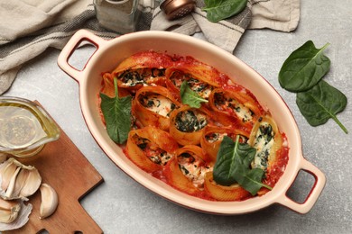 Photo of Delicious conchiglie pasta with ricotta cheese, spinach and tomato sauce in baking dish on gray textured table, flat lay