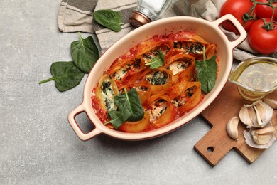 Photo of Delicious conchiglie pasta with ricotta cheese, spinach and tomato sauce in baking dish on gray textured table, flat lay