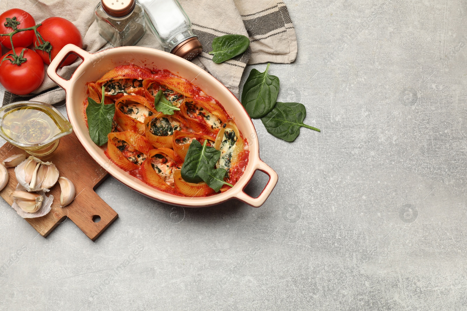 Photo of Delicious conchiglie pasta with ricotta cheese, spinach and tomato sauce in baking dish on gray textured table, flat lay. Space for text