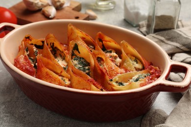 Photo of Delicious conchiglie pasta with ricotta cheese, spinach and tomato sauce in baking dish on gray textured table, closeup