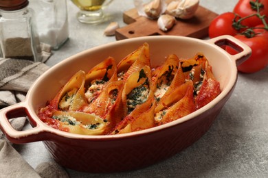 Photo of Delicious conchiglie pasta with ricotta cheese, spinach and tomato sauce in baking dish on gray textured table, closeup