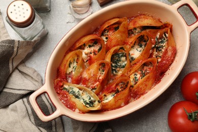 Photo of Delicious conchiglie pasta with ricotta cheese, spinach and tomato sauce in baking dish on gray textured table, flat lay