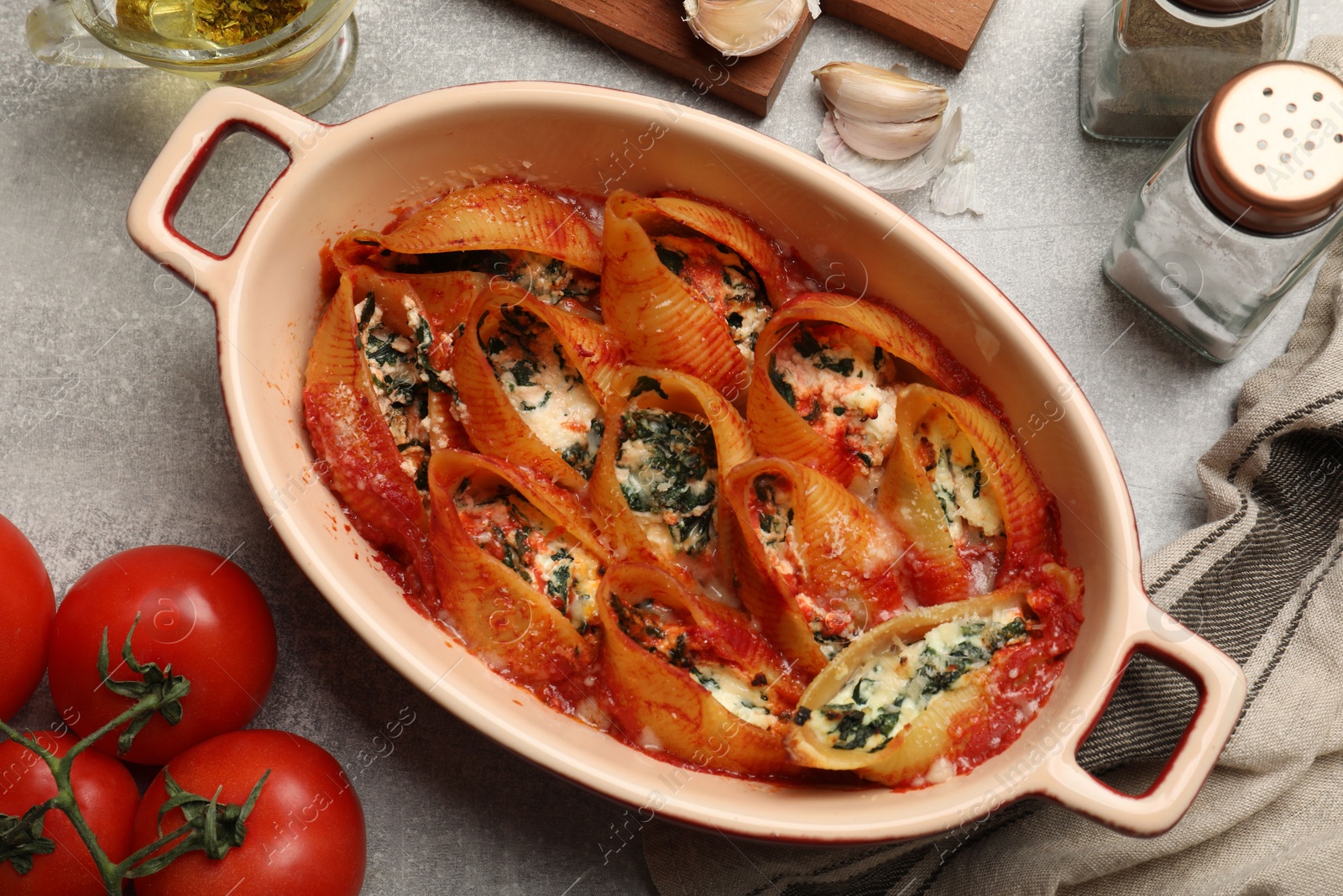 Photo of Delicious conchiglie pasta with ricotta cheese, spinach and tomato sauce in baking dish on gray textured table, flat lay