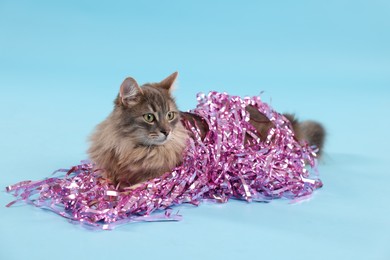 Photo of Cute cat with pink Christmas tinsel on light blue background