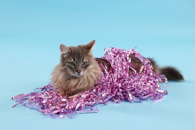 Photo of Cute cat with pink Christmas tinsel on light blue background