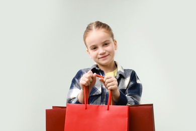 Cute little girl with shopping bags on grey background