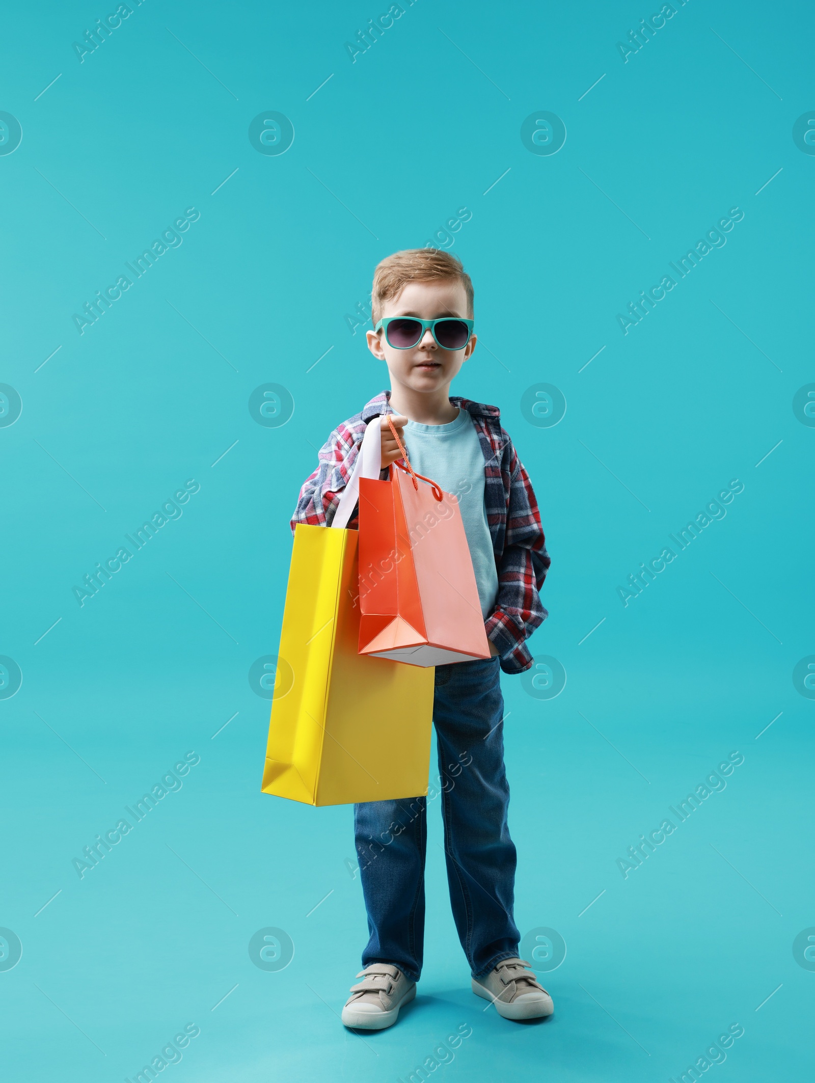 Photo of Cute little boy with shopping bags on light blue background