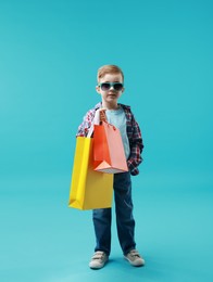 Cute little boy with shopping bags on light blue background