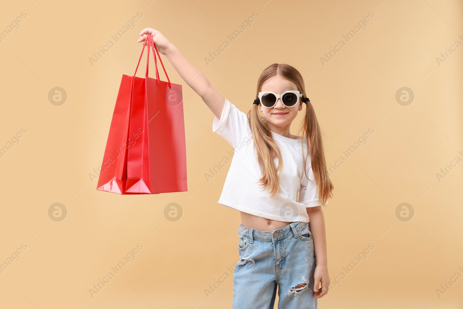 Photo of Cute little girl with shopping bags on beige background