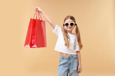 Cute little girl with shopping bags on beige background