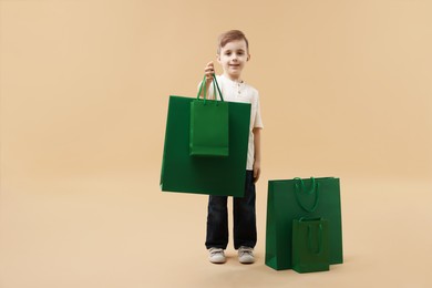 Happy little boy with shopping bags on beige background. Space for text