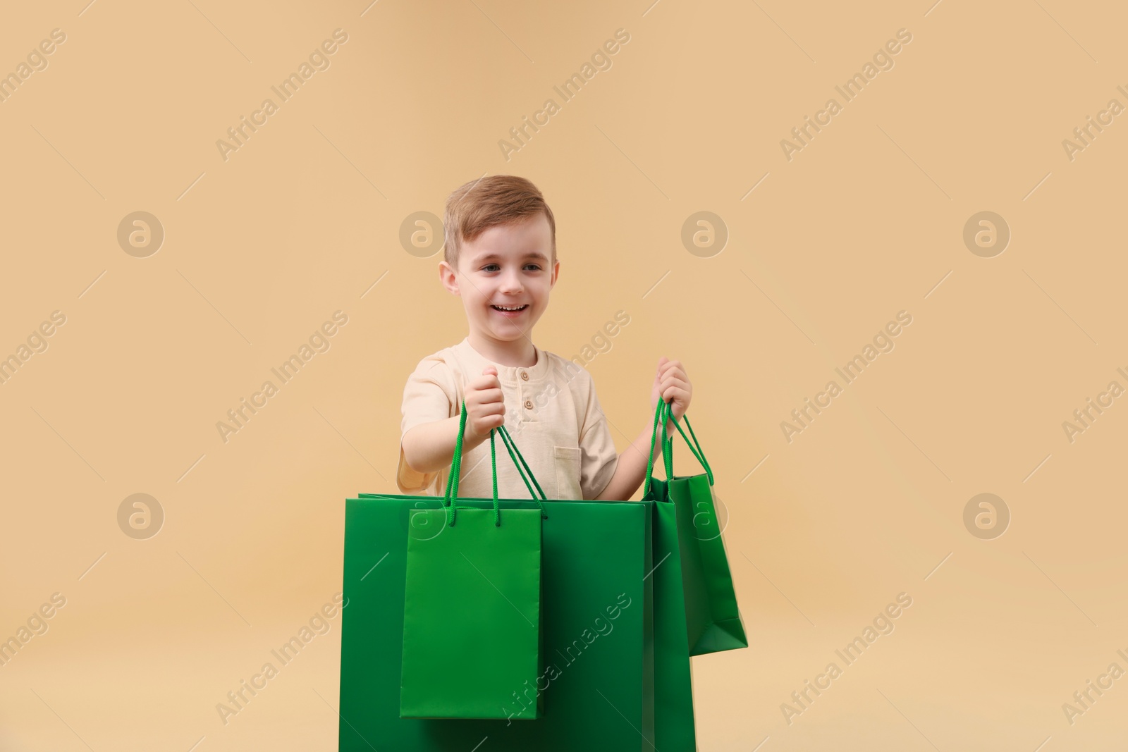 Photo of Happy little boy with shopping bags on beige background