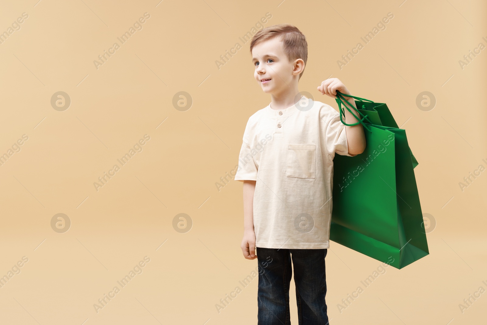 Photo of Happy little boy with shopping bags on beige background. Space for text