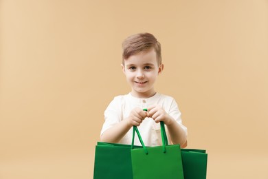 Happy little boy with shopping bags on beige background. Space for text