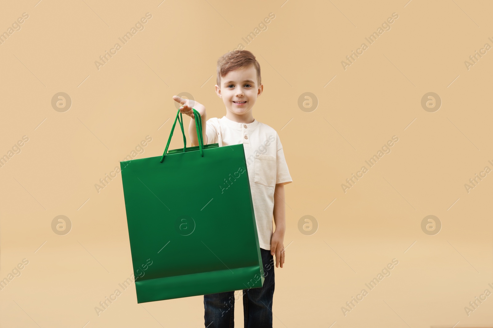 Photo of Happy little boy with shopping bags on beige background. Space for text