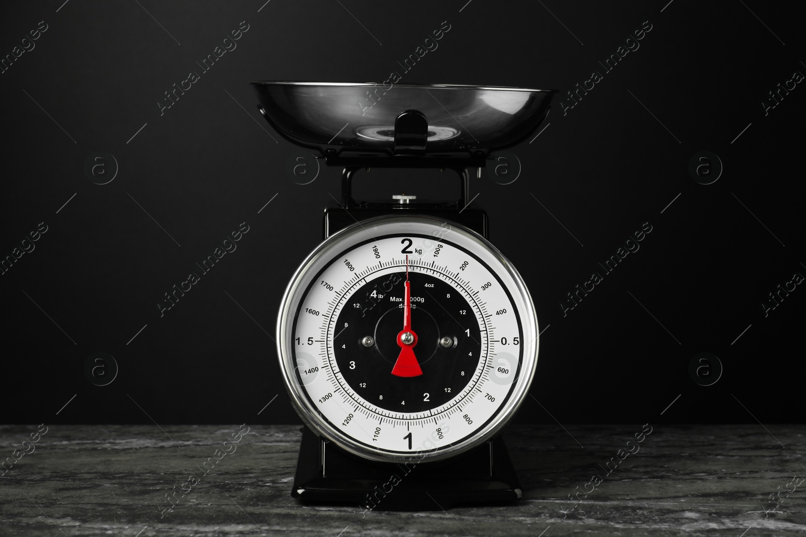 Photo of Mechanical kitchen scale with bowl on dark textured table against black background