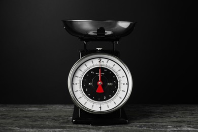 Photo of Mechanical kitchen scale with bowl on dark textured table against black background