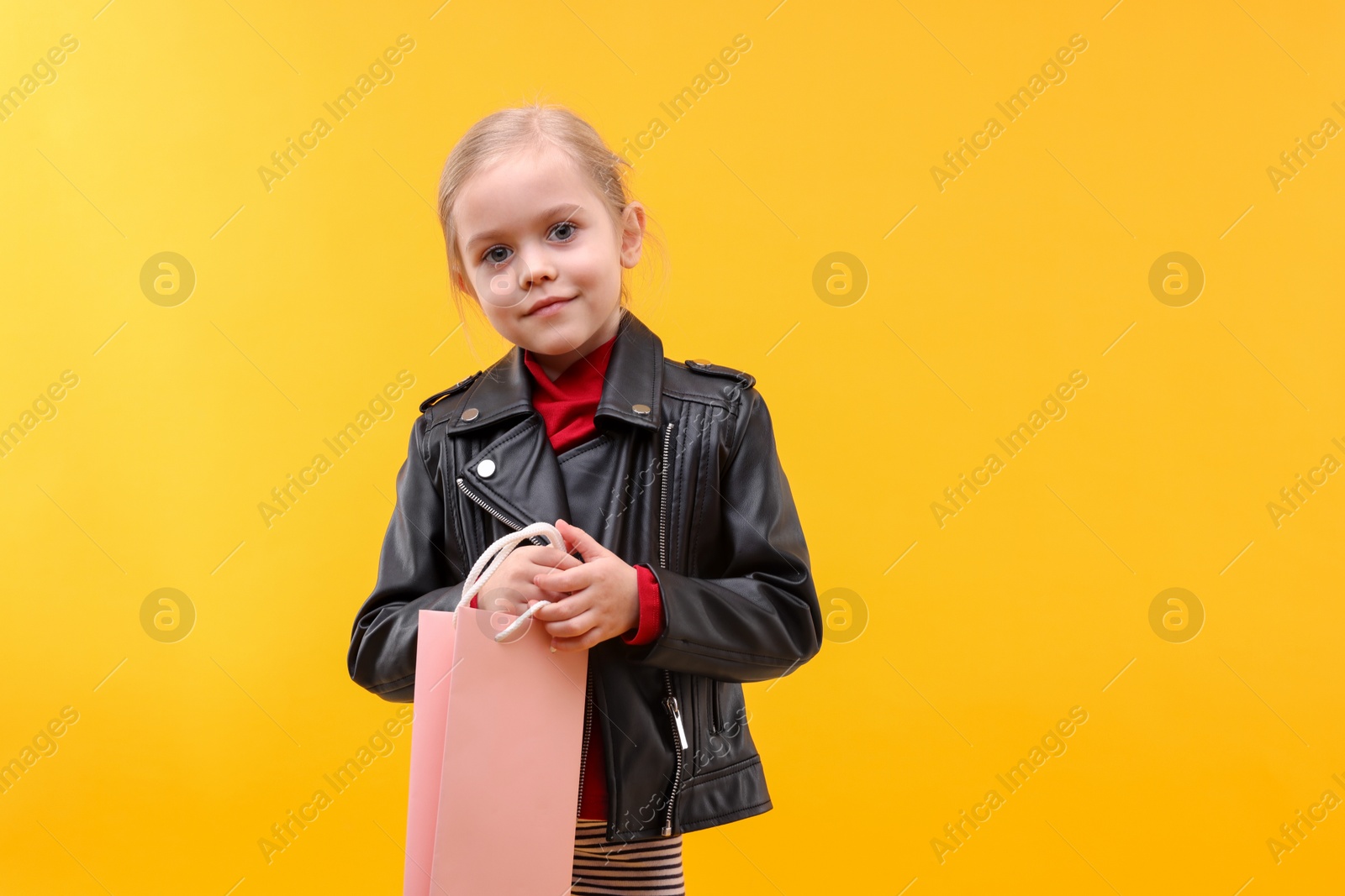 Photo of Little girl with shopping bag on orange background, space for text