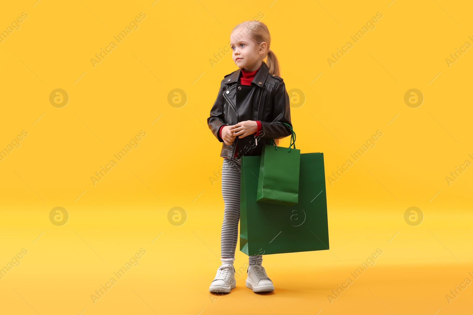 Photo of Little girl with shopping bags on orange background