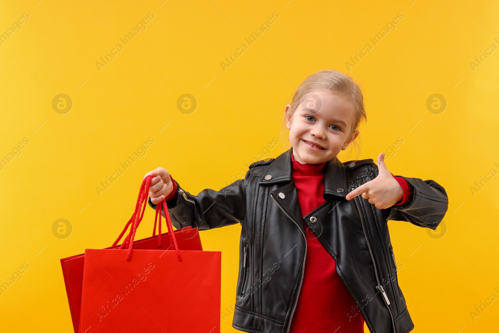 Photo of Little girl pointing at shopping bags on orange background