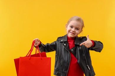 Little girl pointing at shopping bags on orange background