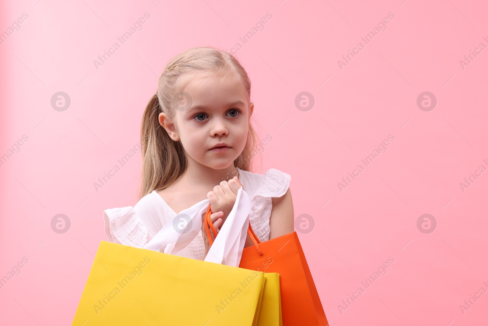 Photo of Little girl with shopping bags on pink background