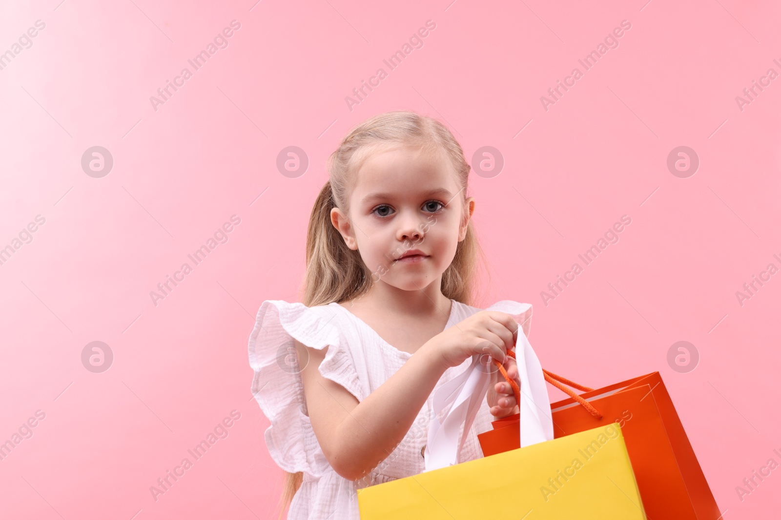 Photo of Little girl with shopping bags on pink background