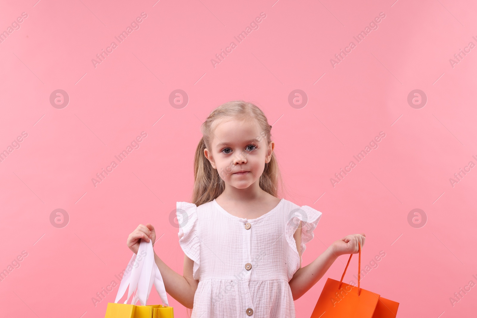 Photo of Little girl with shopping bags on pink background