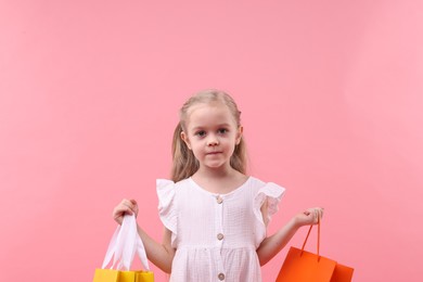 Little girl with shopping bags on pink background