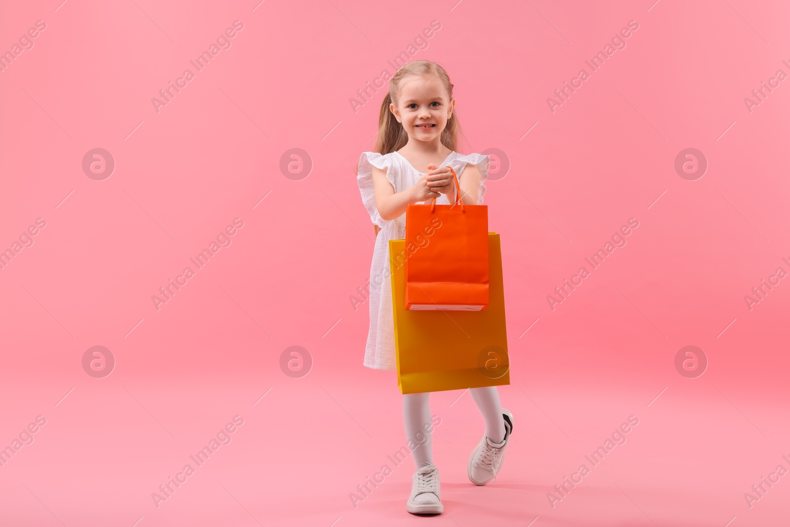 Photo of Little girl with shopping bags on pink background