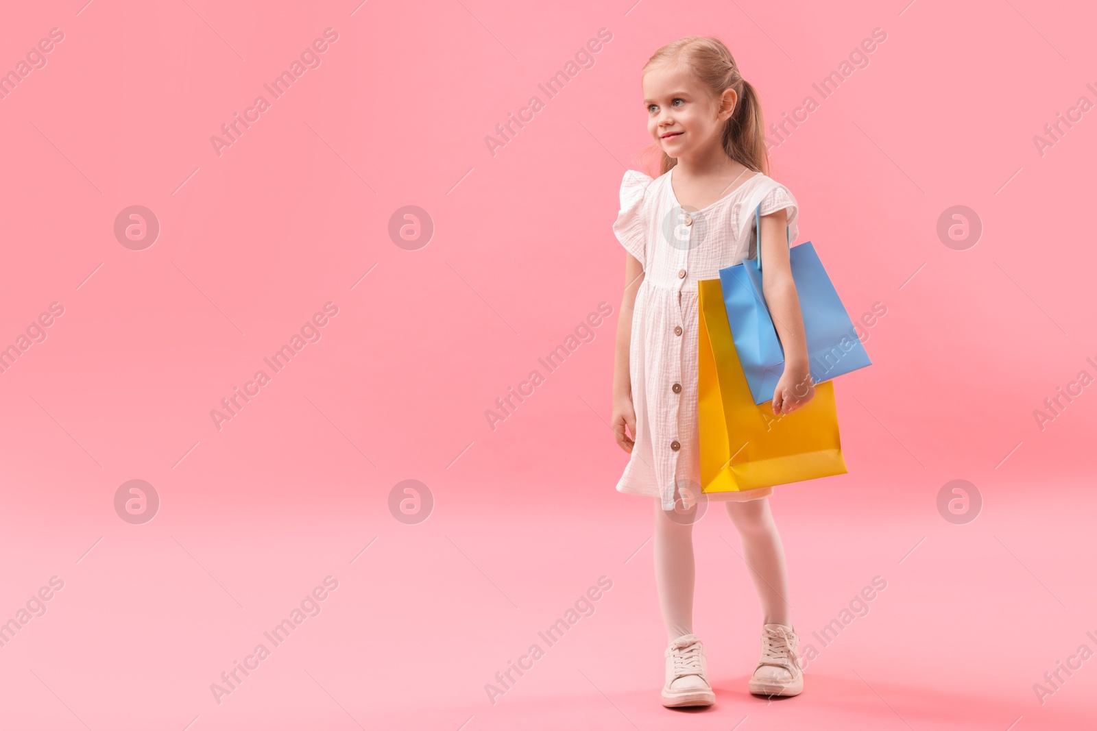 Photo of Little girl with shopping bags on pink background, space for text