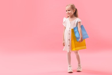 Little girl with shopping bags on pink background, space for text