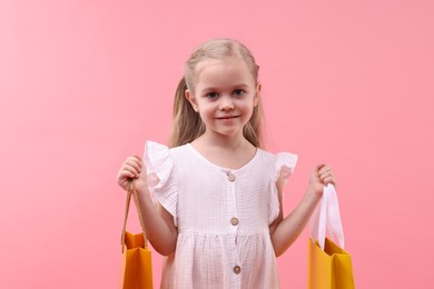 Little girl with shopping bags on pink background