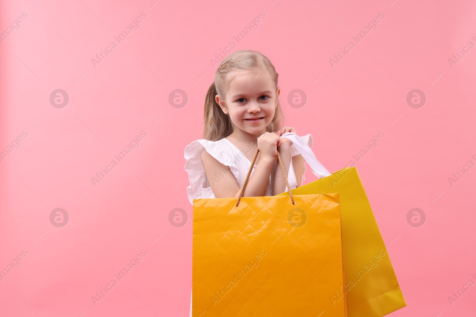 Photo of Little girl with shopping bags on pink background