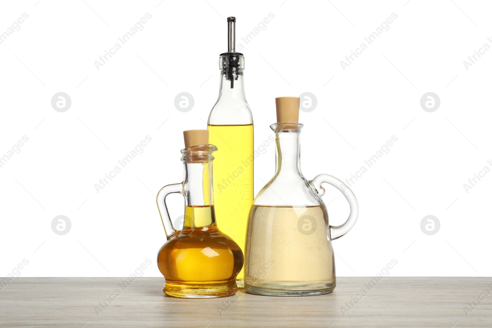 Photo of Oils and vinegar in bottles on wooden table against white background