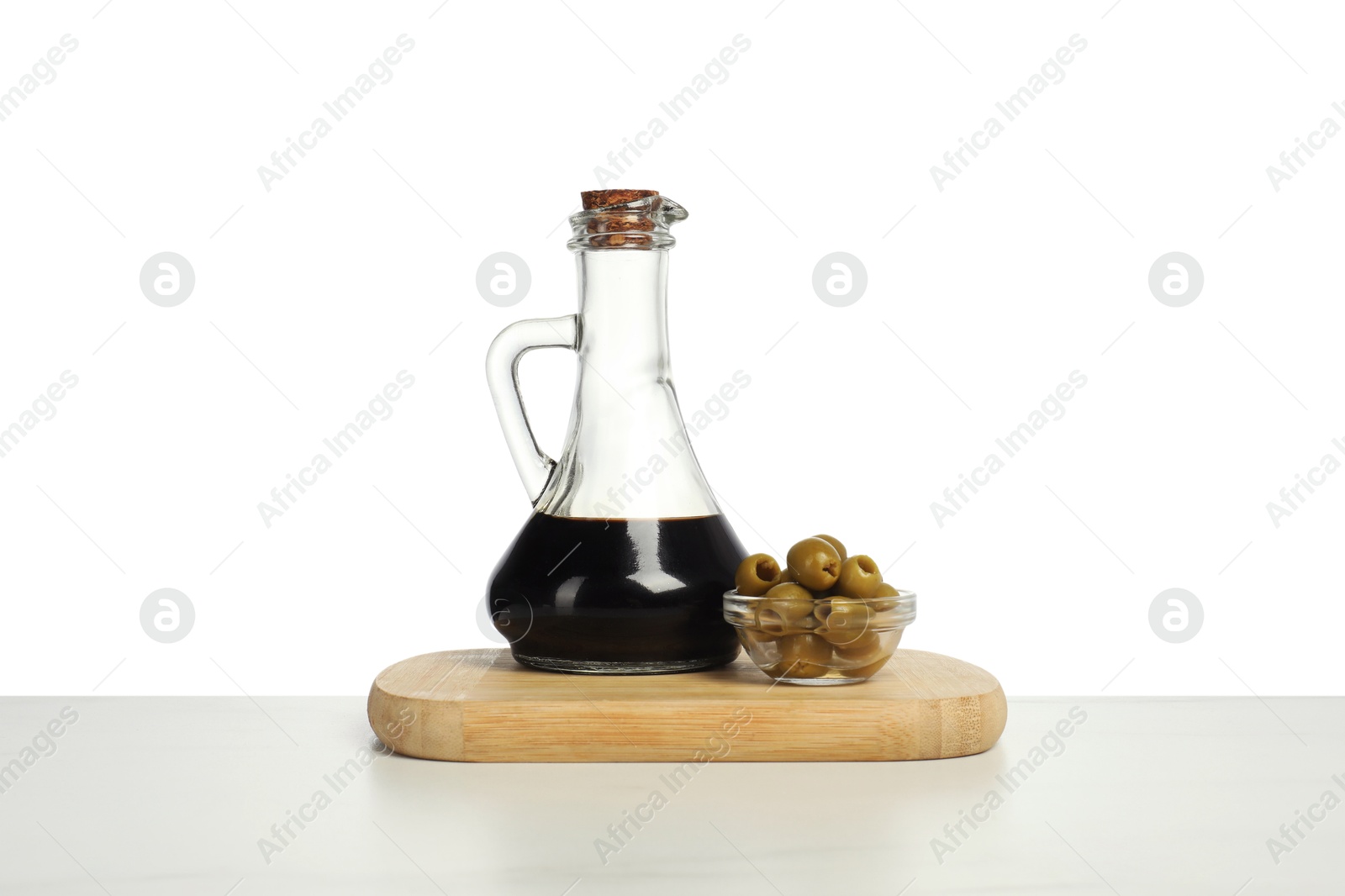 Photo of Vinegar in bottle and olives on table against white background