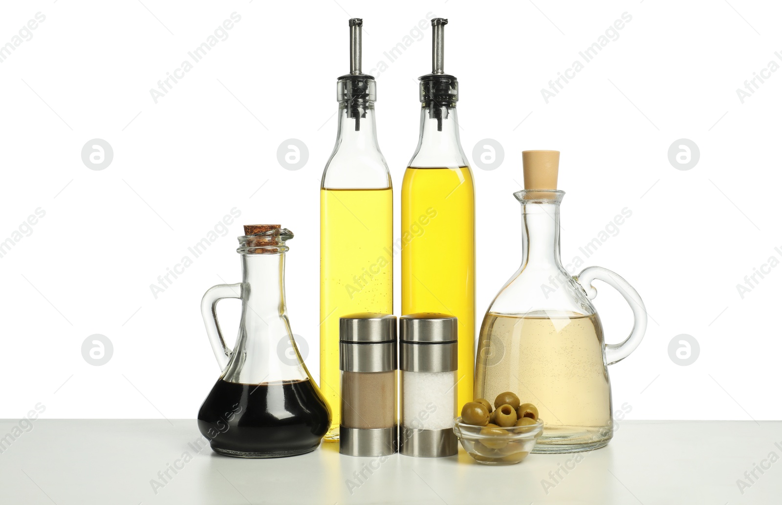 Photo of Salad dressings, spices and olives on table against white background