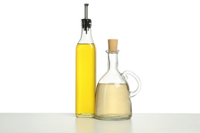 Photo of Oil and vinegar in bottles on table against white background